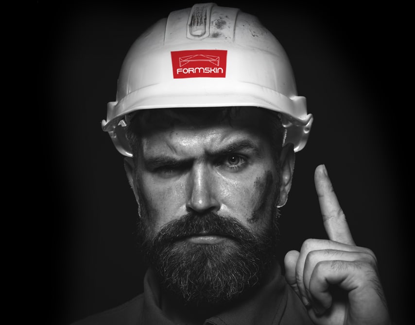 Dyna Products - FormSkin photo of a worker with a beard wearing a hard hat with the FormSkin logo on the front, he uses concrete formwork products like FormSkin.